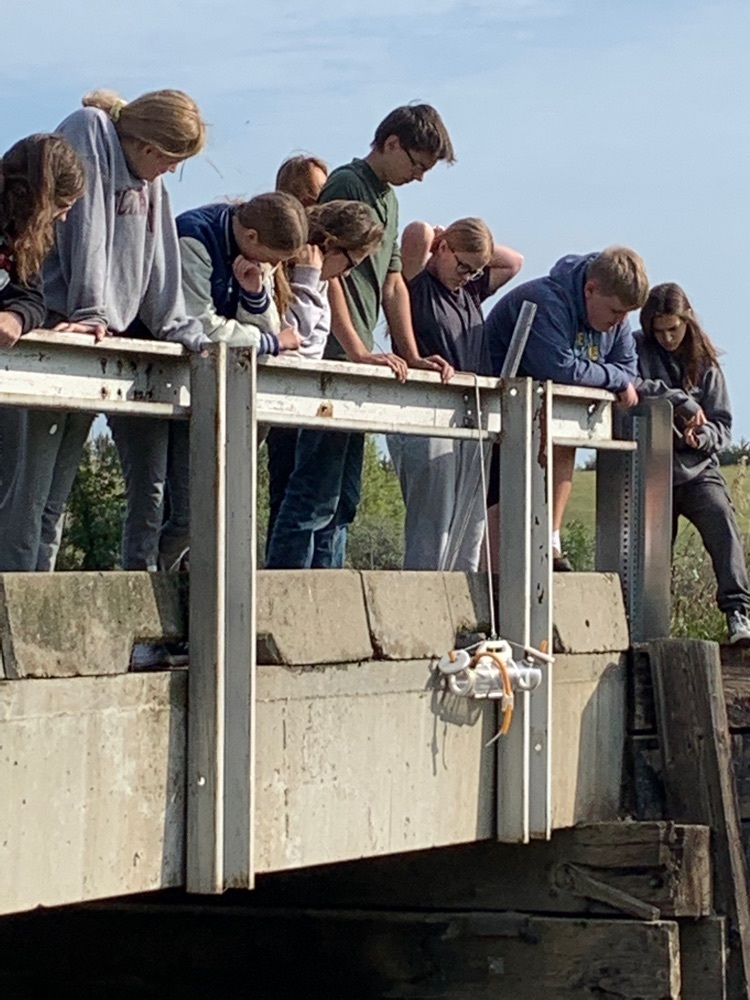 students lowering water collector into creek